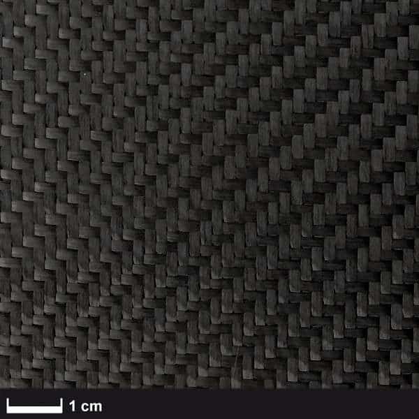 Nærbillede af Kulfibervæv, 200g, twill, 100cm - et tætvævet sort kulfiberstof med et synligt zigzag twill-mønster. En skala på 1 cm viser vævestørrelsen. Ideelt til marineprojekter. Mere info på boatkitshop.com.