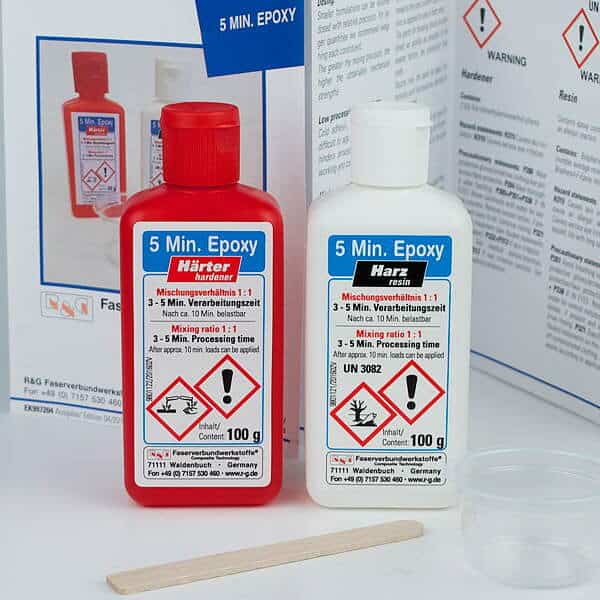 To flasker 5 min epoxylim (rød hærder og hvid resin) med advarselsmærkater står side om side. Foran ligger en mikserpind i træ fra boatkitshop.com, og i baggrunden ligger et instruktionsark.