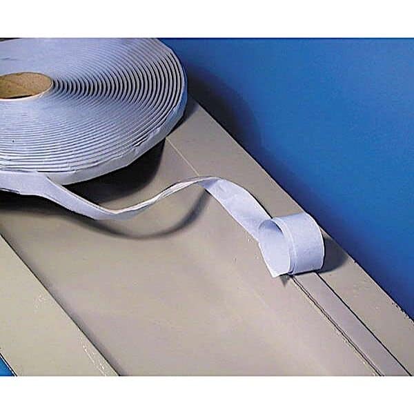 En rulle Vakuum forseglingstape 90 °C ligger på en beige overflade mod en blå væg, med en længde af den hvide selvklæbende skumtape delvist udrullet og krøllet.